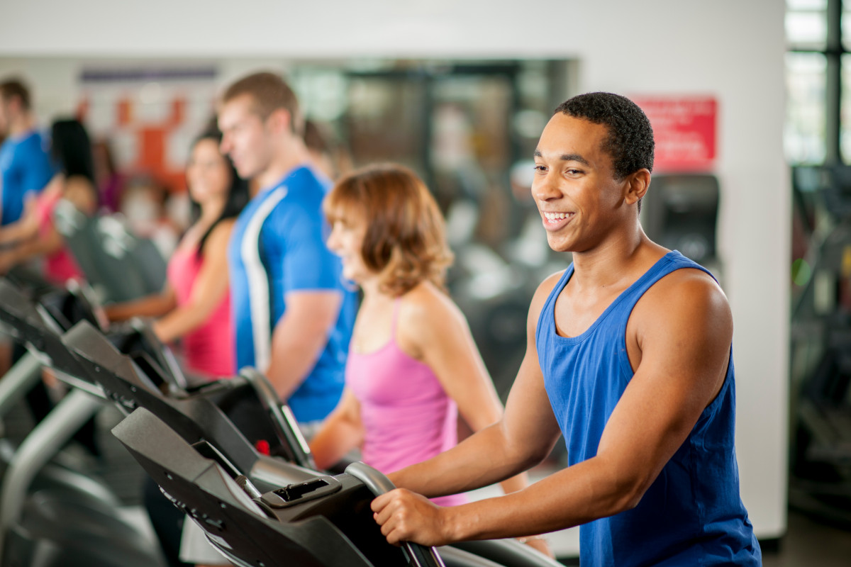 A multi-ethnic group of young adults are in a row at the gym on workout machines.